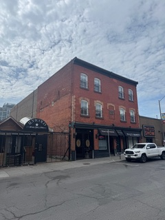 Red brick building with a bar on the ground floor, a truck parked on the street, and a cloudy sky overhead.