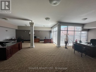Spacious office interior with desks and a large window. Beige carpet and gray walls, some decorative columns.