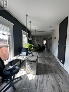 An office space with a desk, chair, and long hallway. Dark accent wall with light-colored flooring and windows.