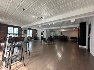 Spacious loft with hardwood floors, brick wall, and a decorative white ceiling. Includes bar seating and lounge furniture.