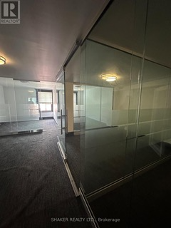 Interior view of an empty office space with glass walls and dark carpet. The lighting is dim.