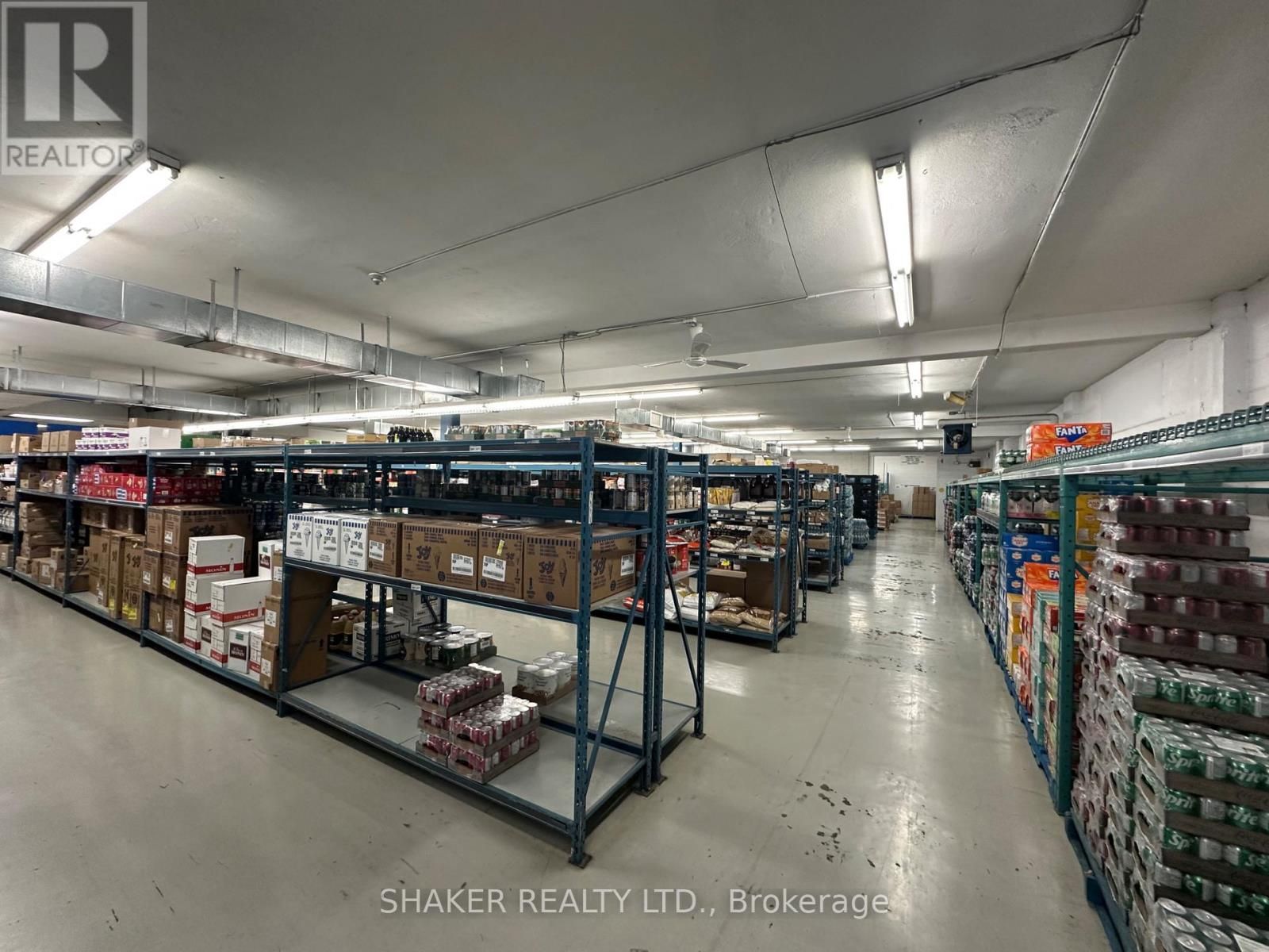 Warehouse interior with rows of metal shelves stocked with various packaged goods. Fluorescent lighting.