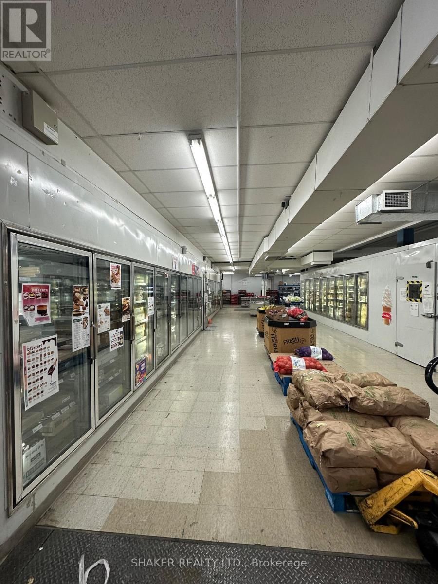 Interior view of a grocery store aisle with freezers, shelves, and pallets of goods.