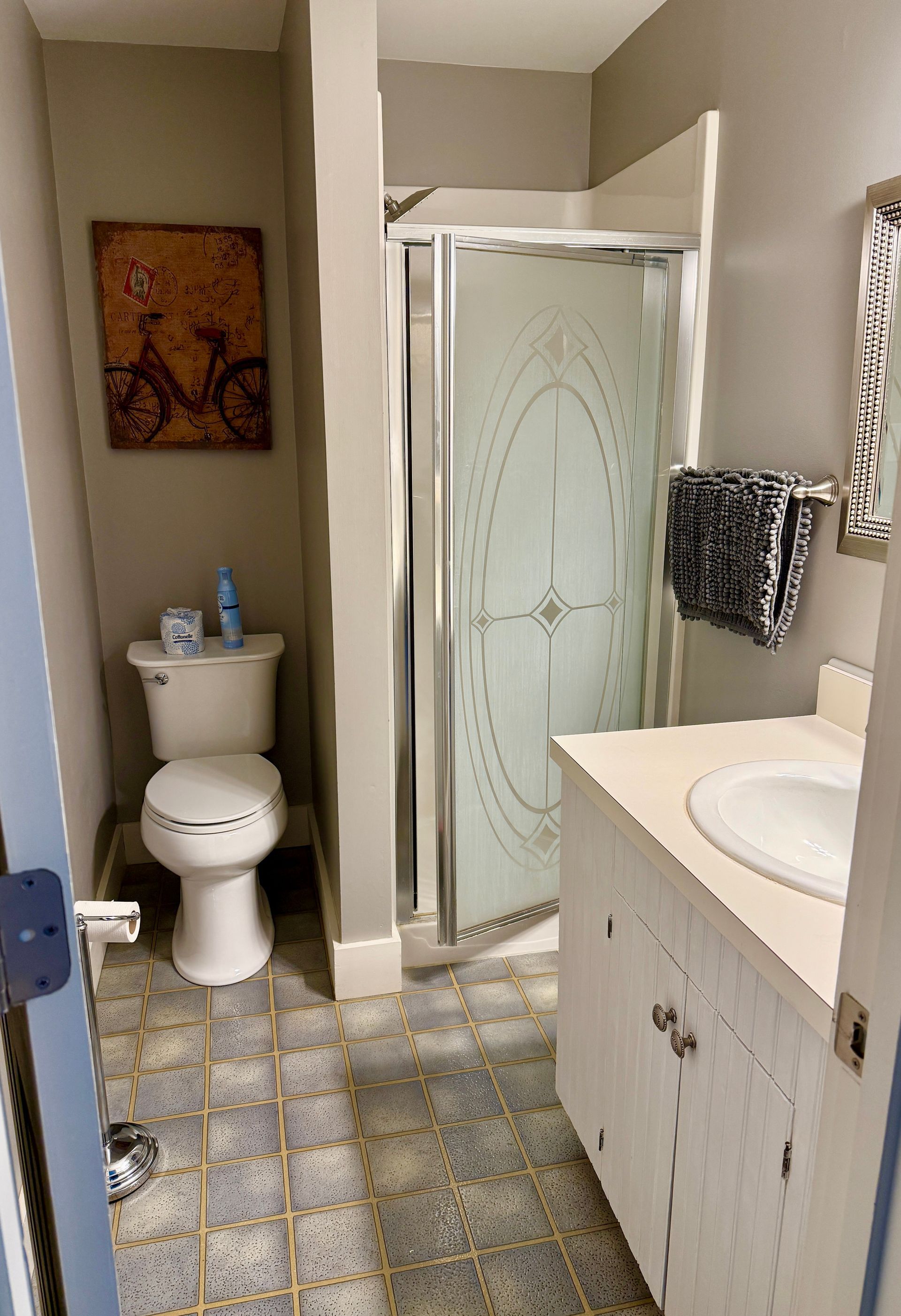 Bathroom with toilet, shower, vanity, and a framed art piece; light grey walls, tile floor.