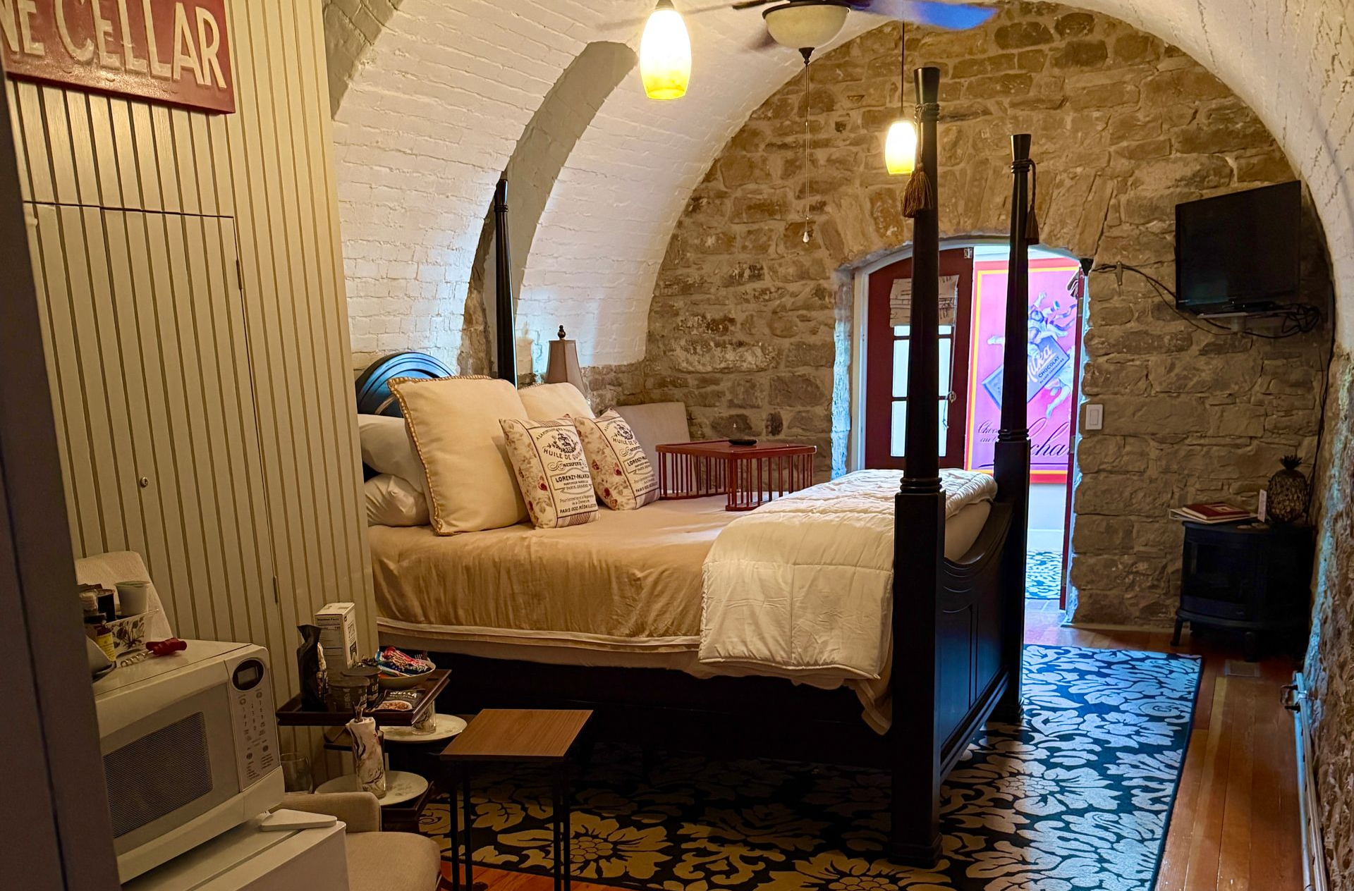 Bedroom with arched stone ceiling, four-poster bed, and colorful tiled floor leading to an open doorway.