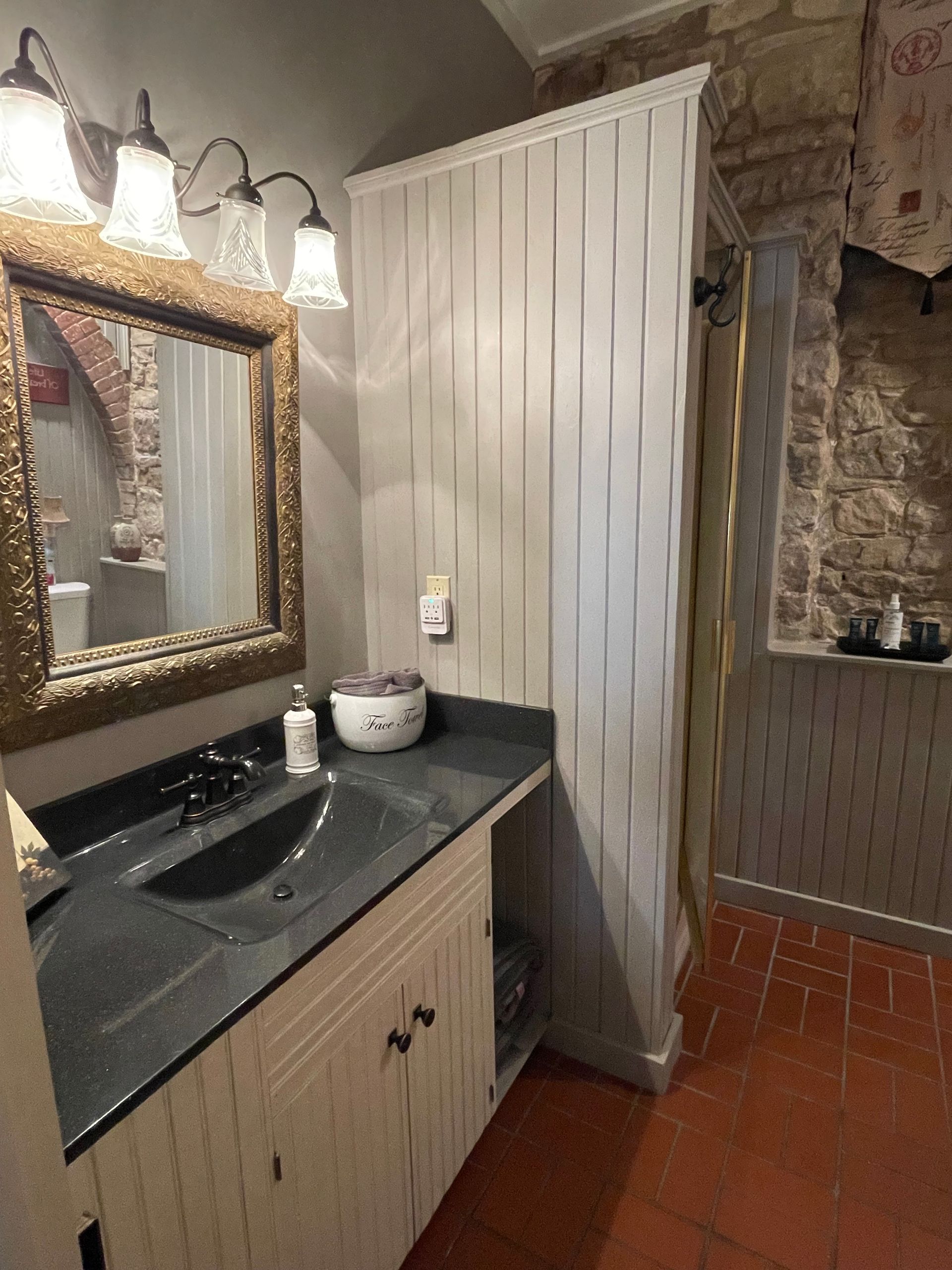 Bathroom with vanity, mirror, beadboard wall, and shower. Brick floor.