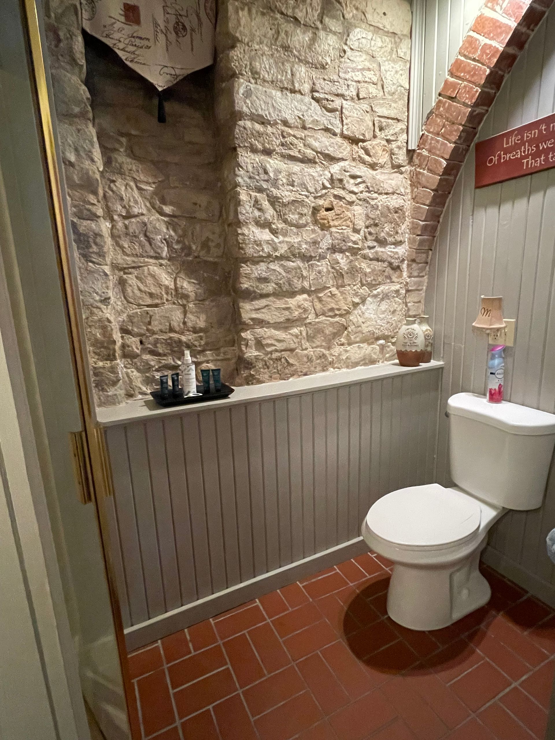 A small bathroom with a stone wall and brick floor. A toilet sits next to a panelled wall.