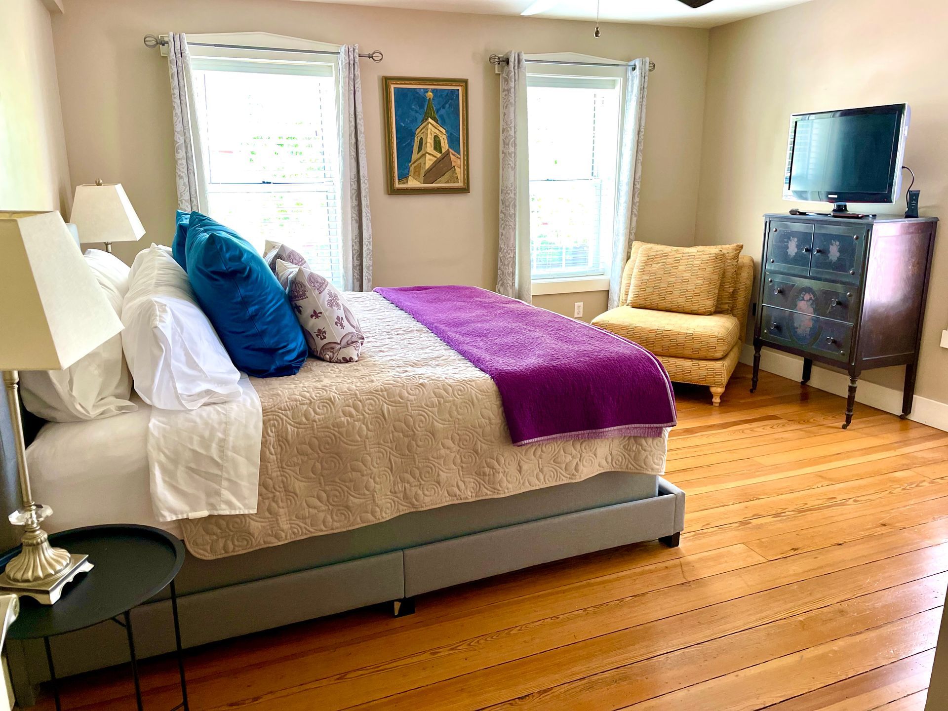 Bedroom with a bed, armchair, dresser, two windows, and hardwood floors.