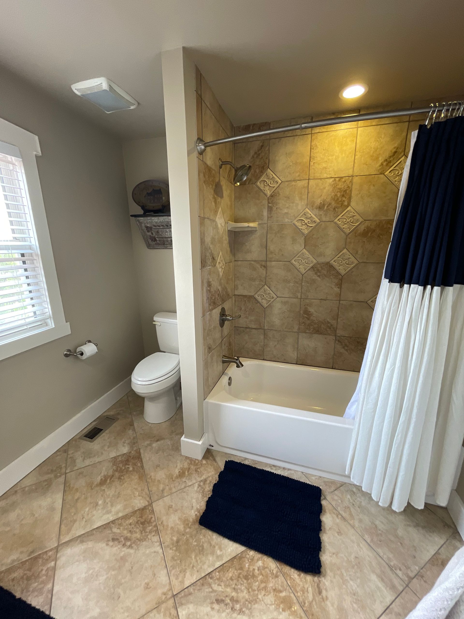 Bathroom with tiled floor and shower, toilet, window, and navy and white shower curtain.