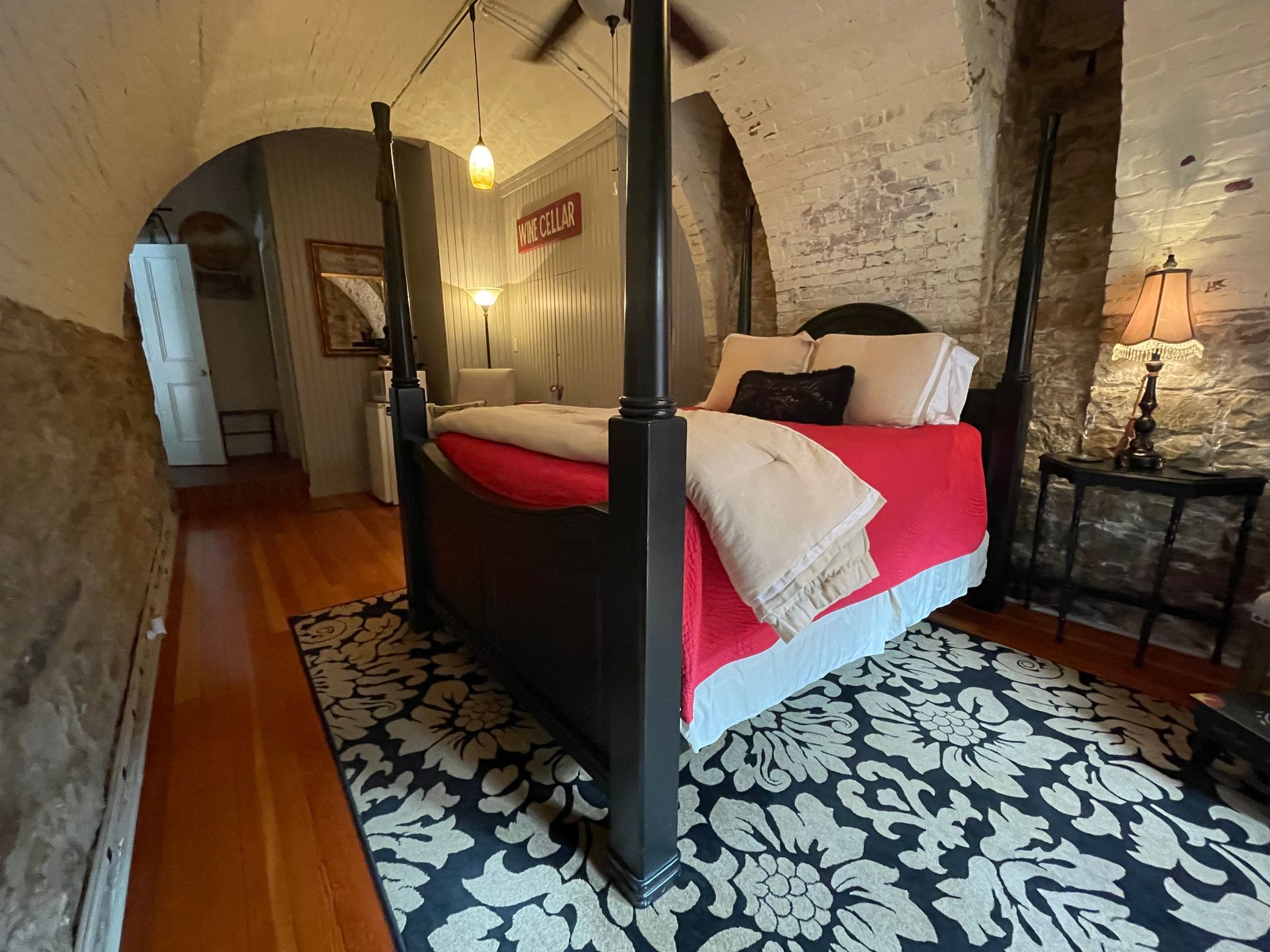 Bedroom with four-poster bed, red bedding, black rug, and stone walls.