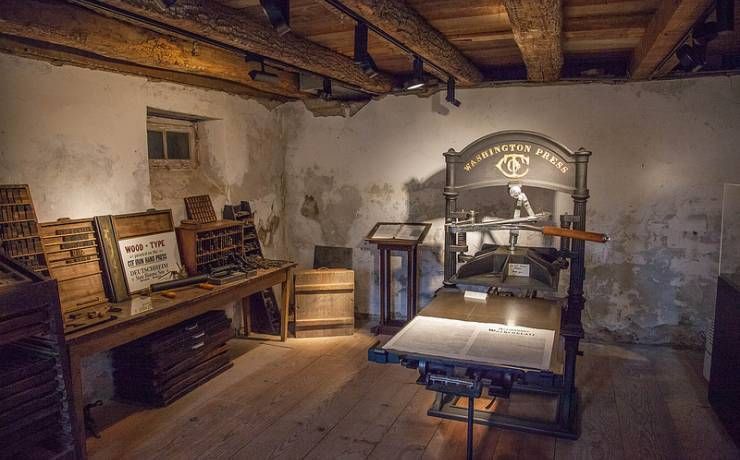 Old printing press in a rustic room with wooden beams and a large press.
