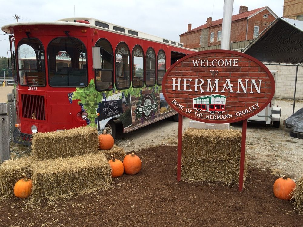 Red trolley in Hermann, Missouri, with welcome sign, hay bales, and pumpkins.