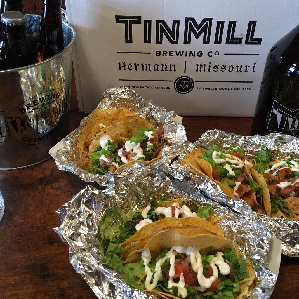 Tacos on foil next to a Tin Mill Brewing Co. bag and beer bottles in a bucket.