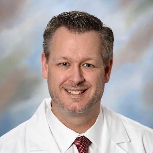 A smiling doctor in a lab coat with a stethoscope around his neck.