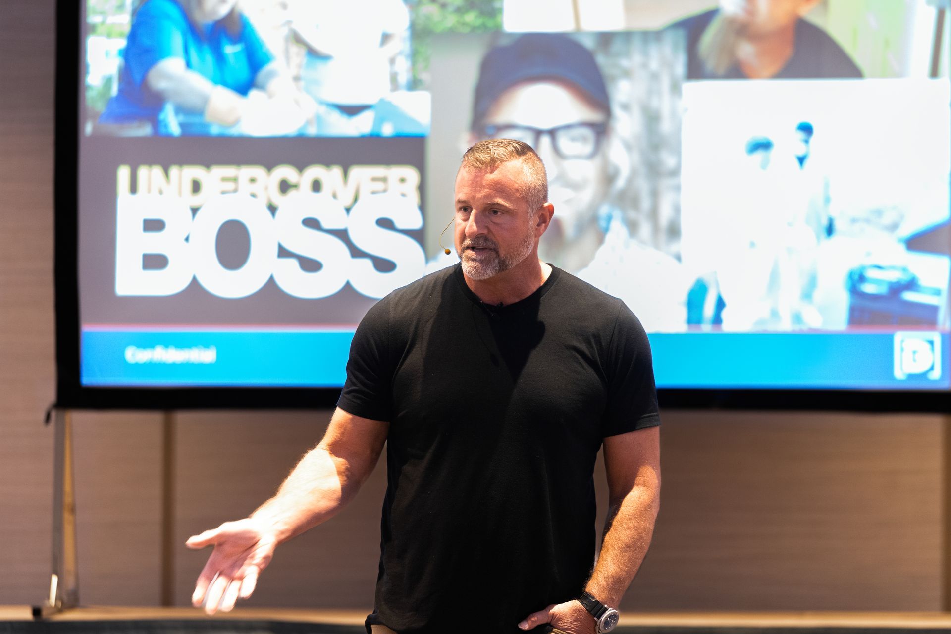 A man is standing in front of a large screen that says undercover boss.