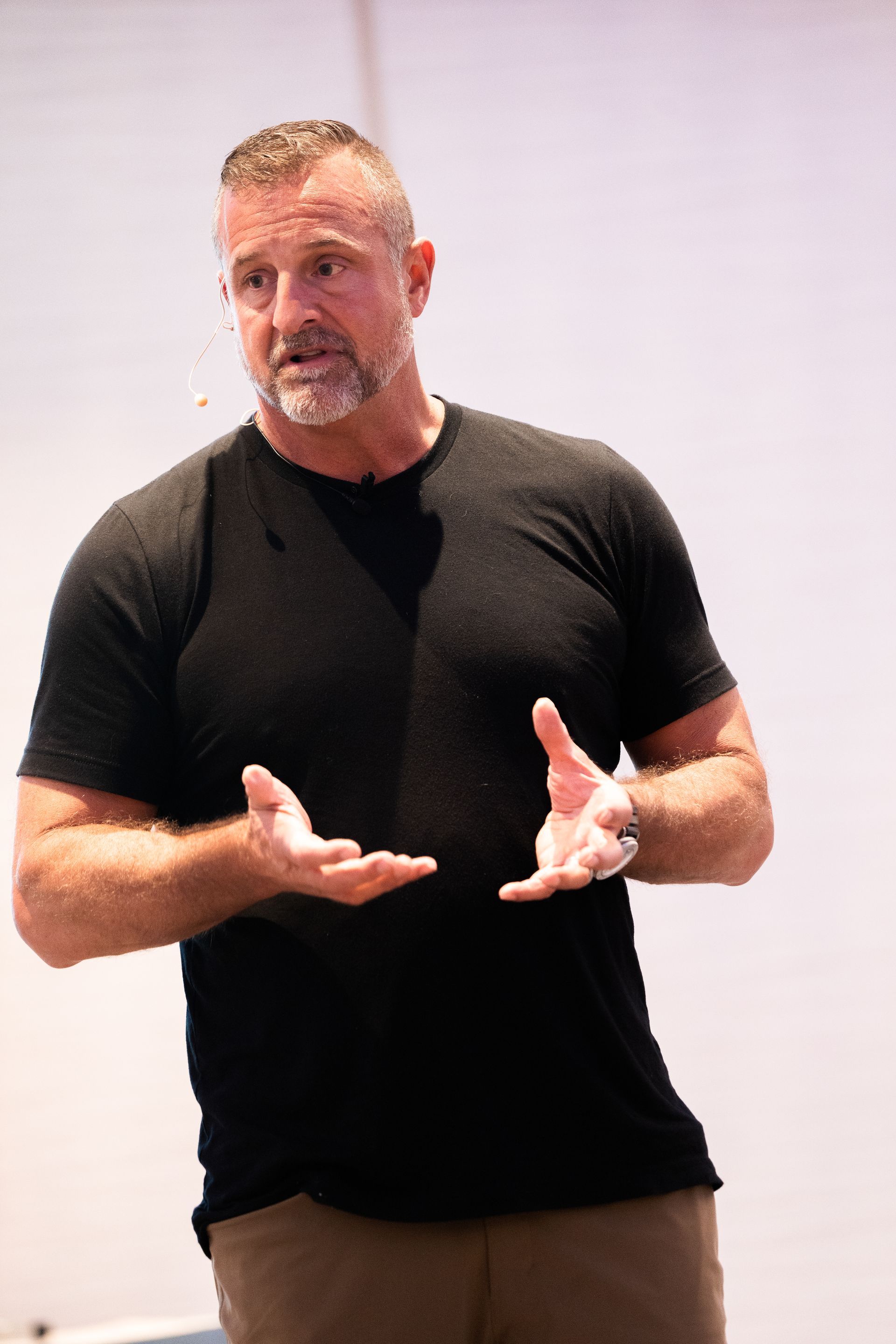 A man with a beard is standing in front of a white wall with his hands outstretched.