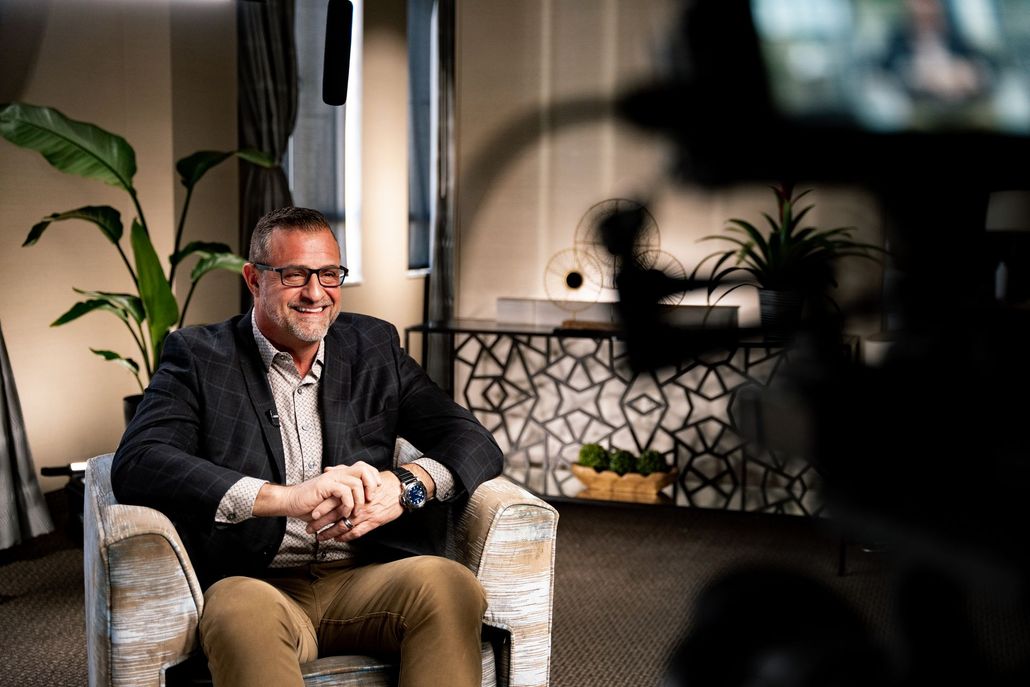A man is sitting in a chair in front of a camera.