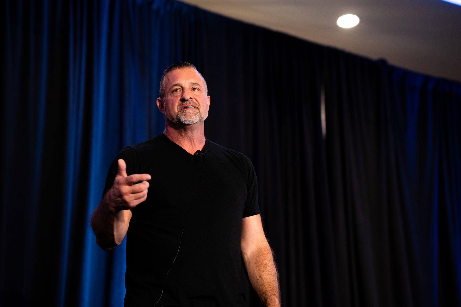 A man in a black shirt is standing on a stage giving a speech.