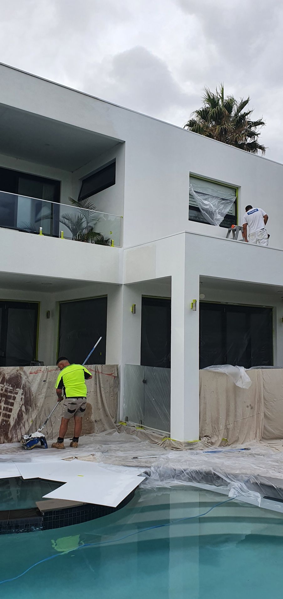 A man is painting a large white house next to a pool.