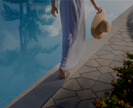 A woman is walking by a swimming pool holding a hat.