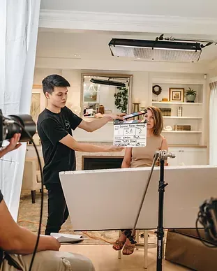 A man is holding a clapper board in front of a woman sitting on a couch.