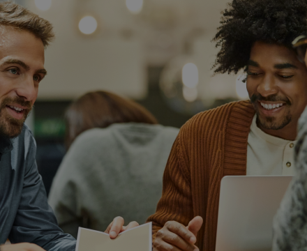 A group of men are sitting at a table looking at a laptop.
