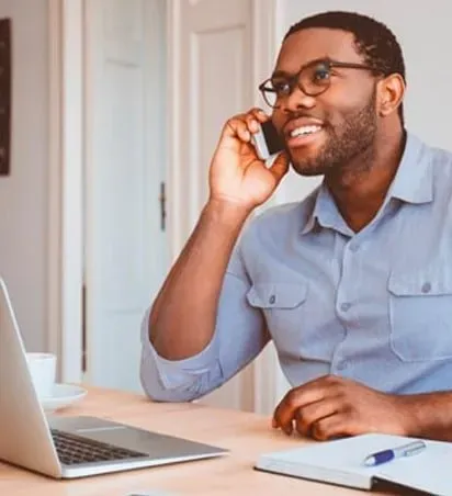 A man is sitting at a desk talking on a cell phone.
