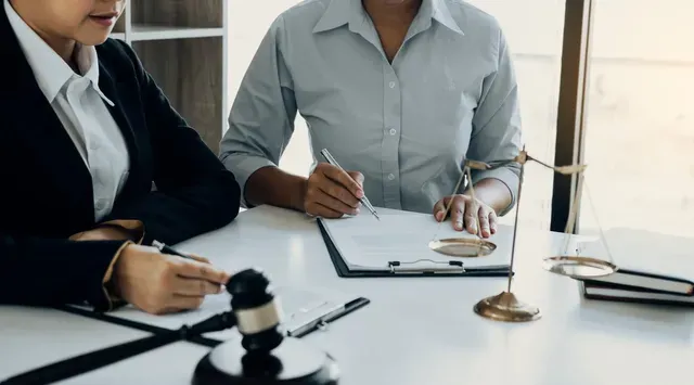 Two women are sitting at a table signing a document.