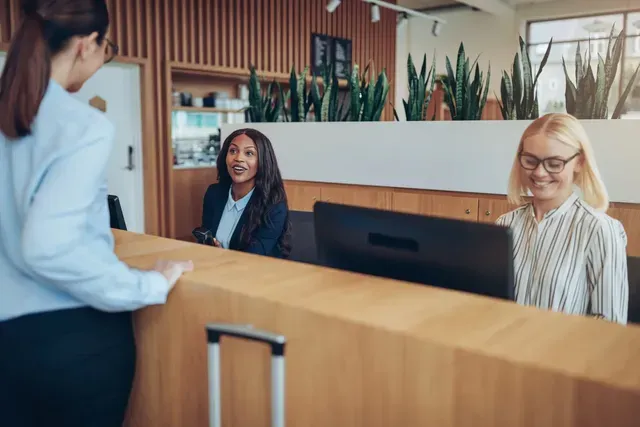 Two women are standing at a hotel reception desk.