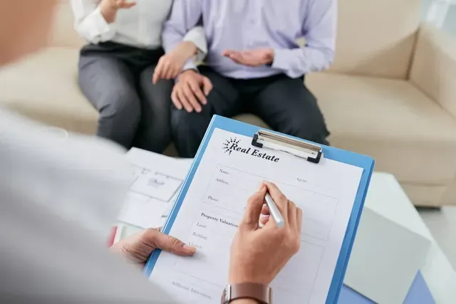 A man and woman are sitting on a couch with a clipboard in front of them.