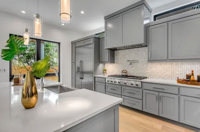 Modern gray kitchen with white countertops, stainless steel appliances, and gold accents.