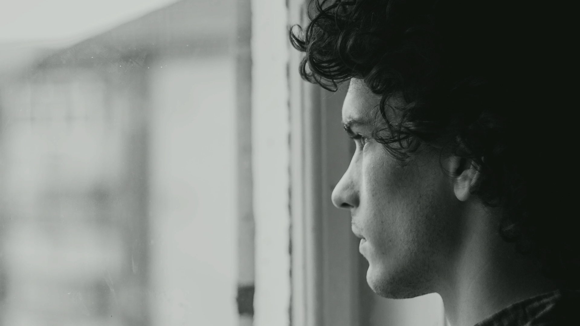 a black and white photo of a man looking out of a window representing suicide and self harm at Healing Our Trauma KC background .