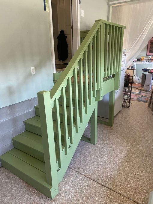 A green wooden staircase with a green railing in a room.