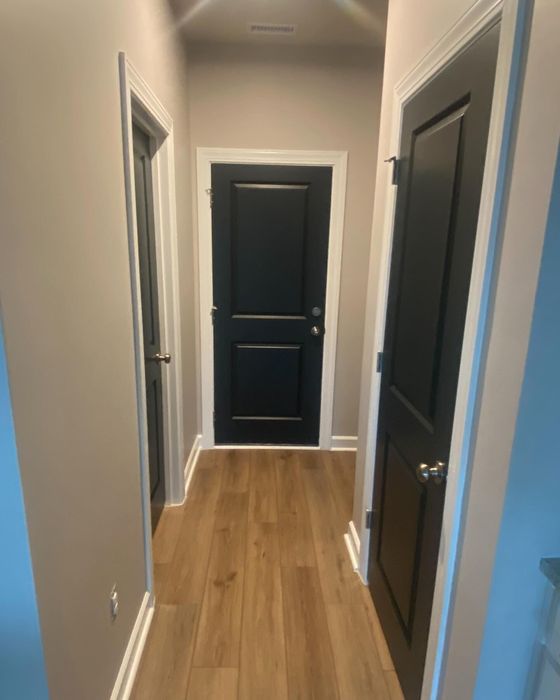 A hallway with hardwood floors and a black door.