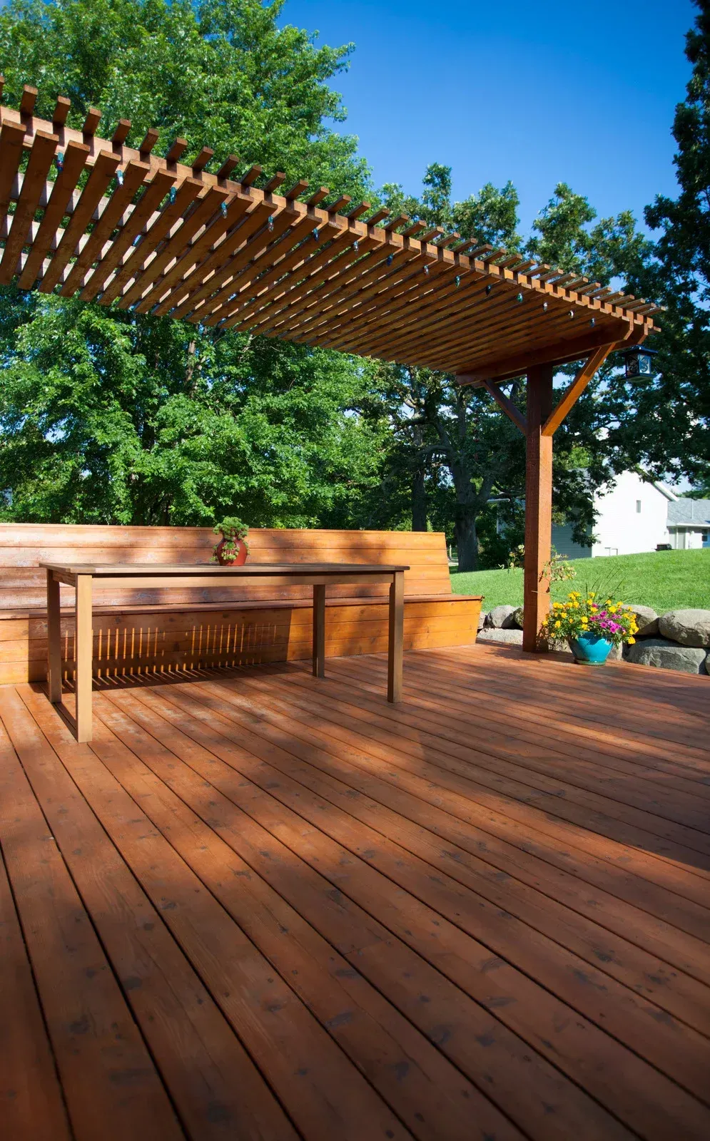 A wooden deck with a table and bench under a pergola.