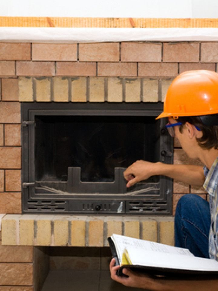 A man wearing an orange hard hat is working on a fireplace.
