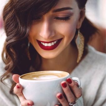 Una mujer sonríe mientras sostiene una taza de café.