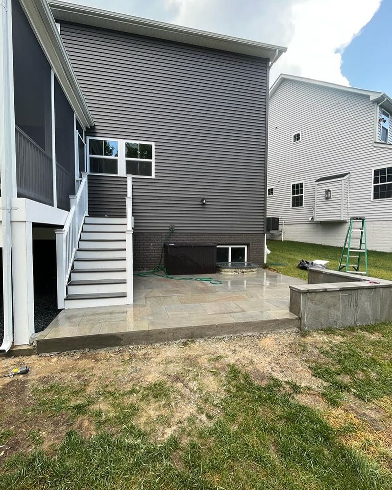 Backyard patio with gray house, stairs, and retaining wall.