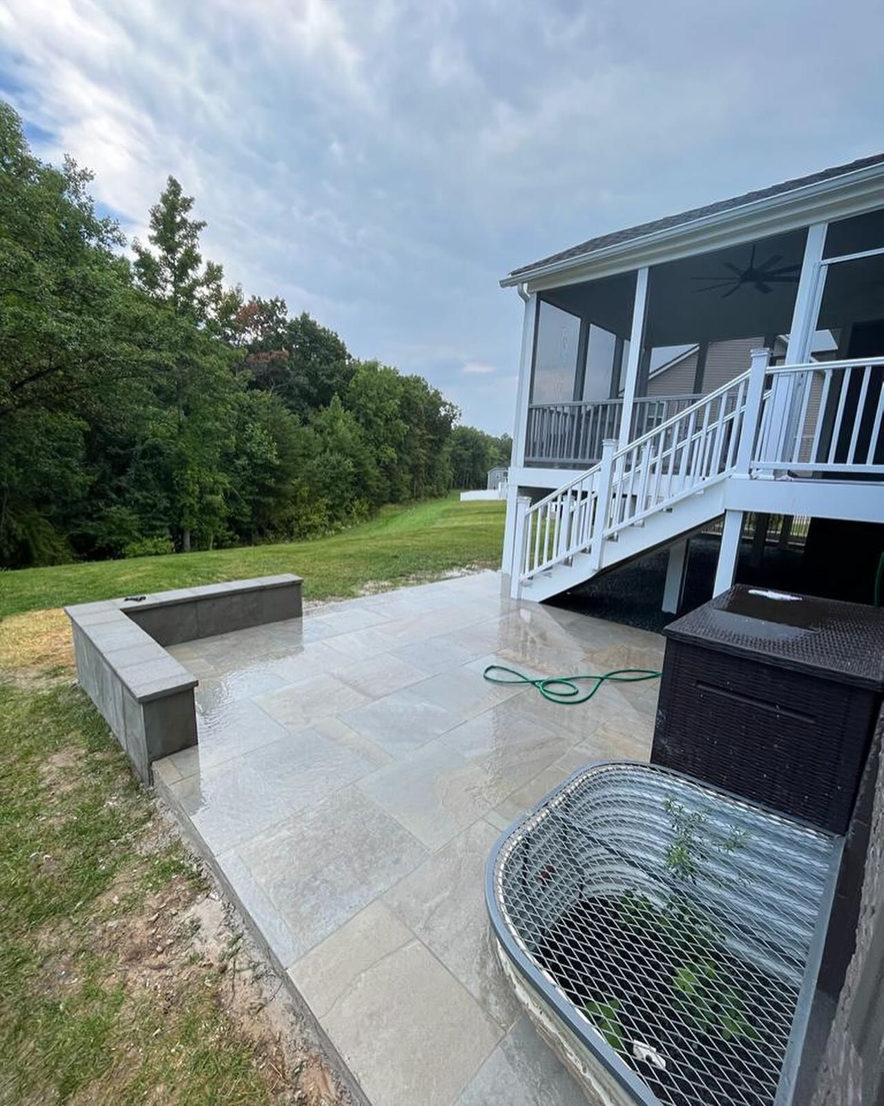 Outdoor patio next to a house with a staircase, stone pavers, and a retaining wall, under a cloudy sky.