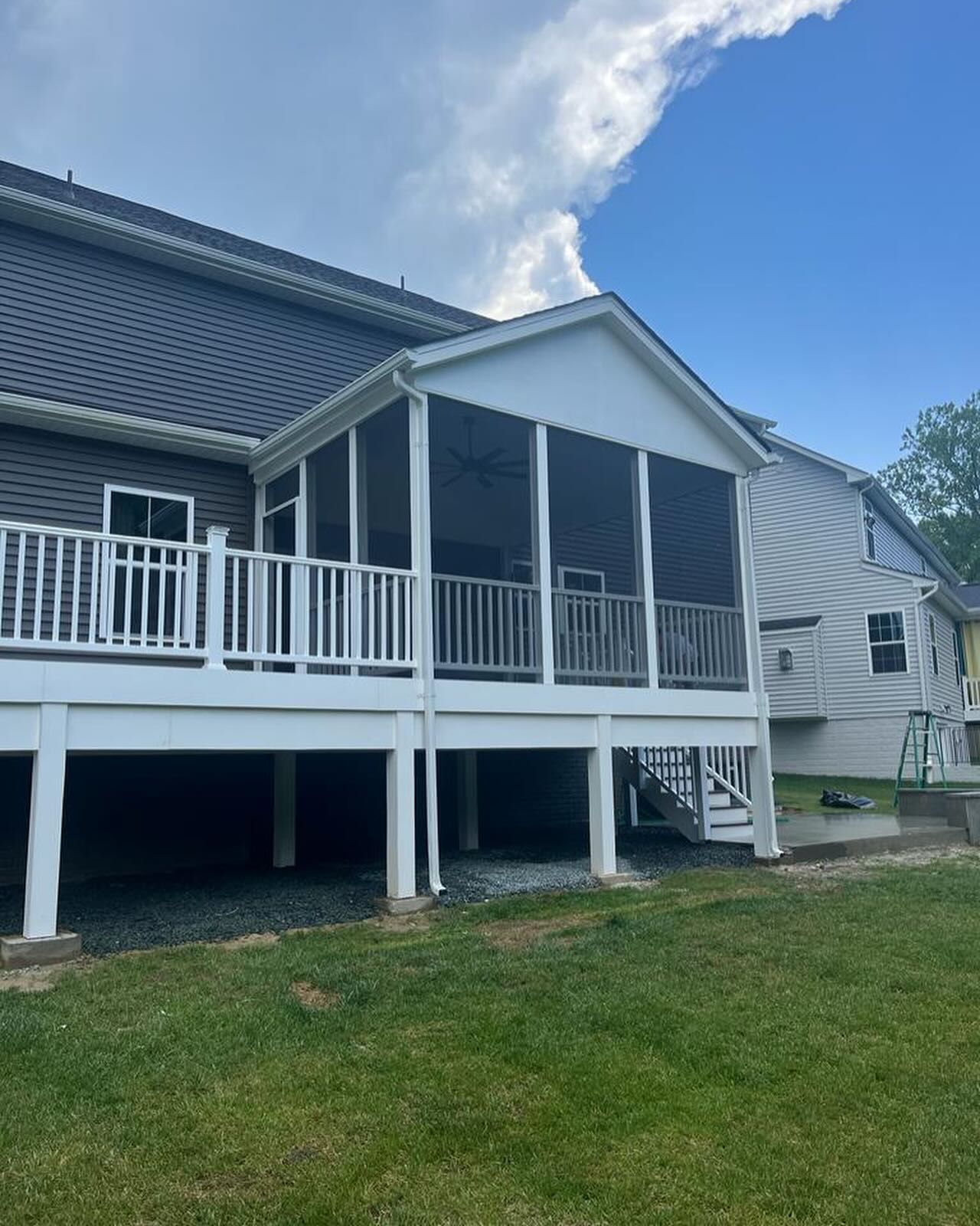 White screened porch and deck attached to a gray house, with a blue sky.