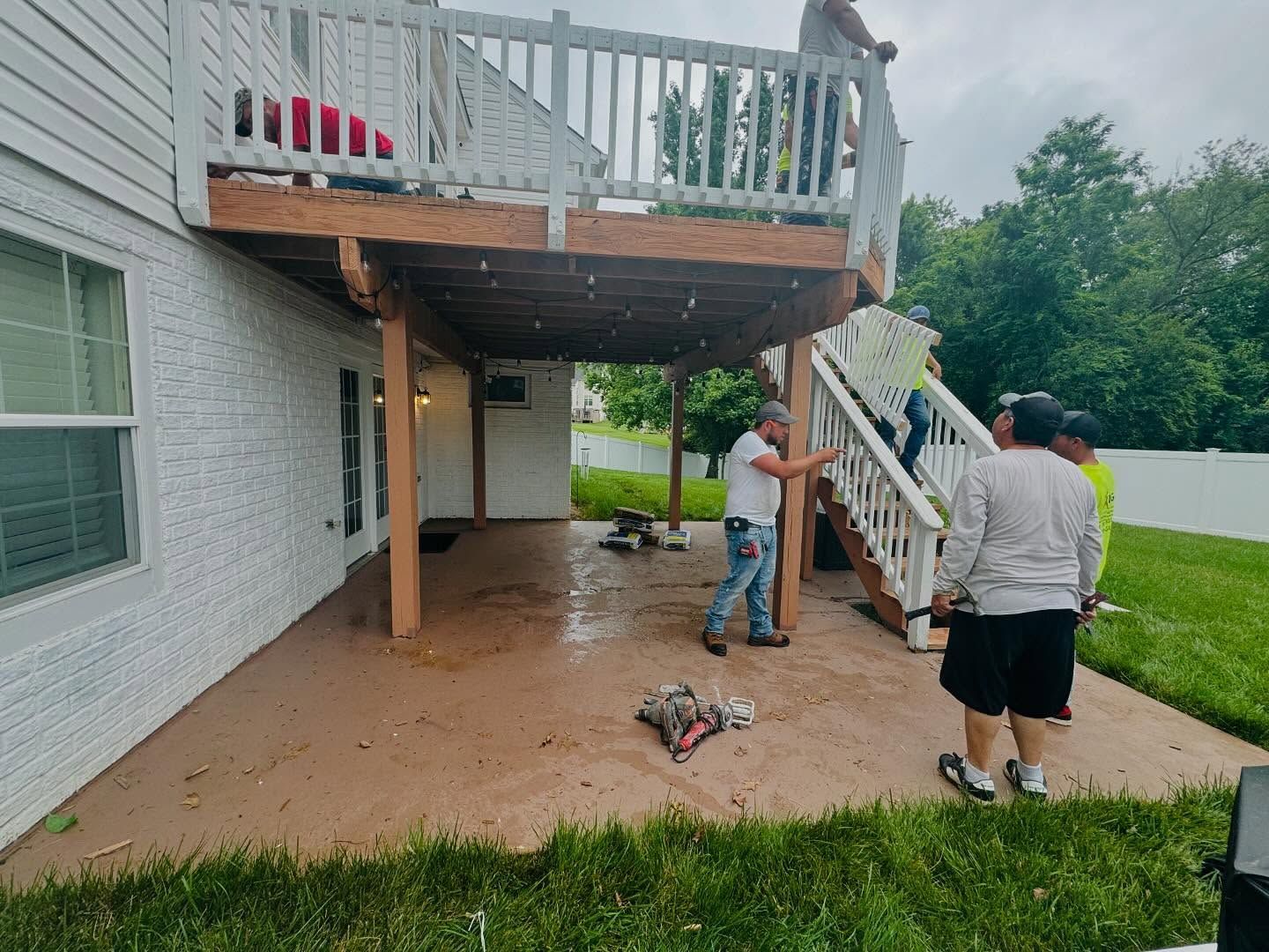 Workers constructing a wooden deck with a covered patio on a residential property.
