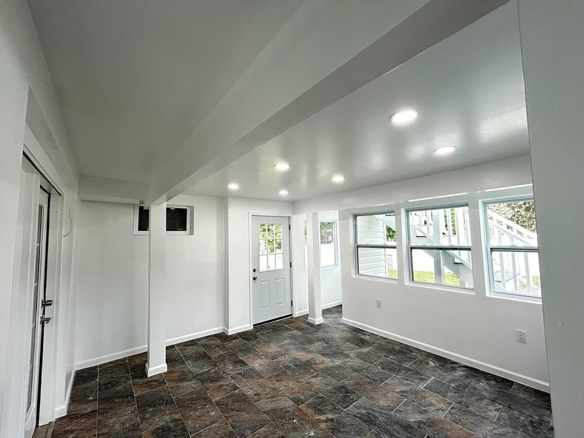 Interior view of a white-walled room with a dark patterned floor, featuring windows, a door, and recessed lighting.
