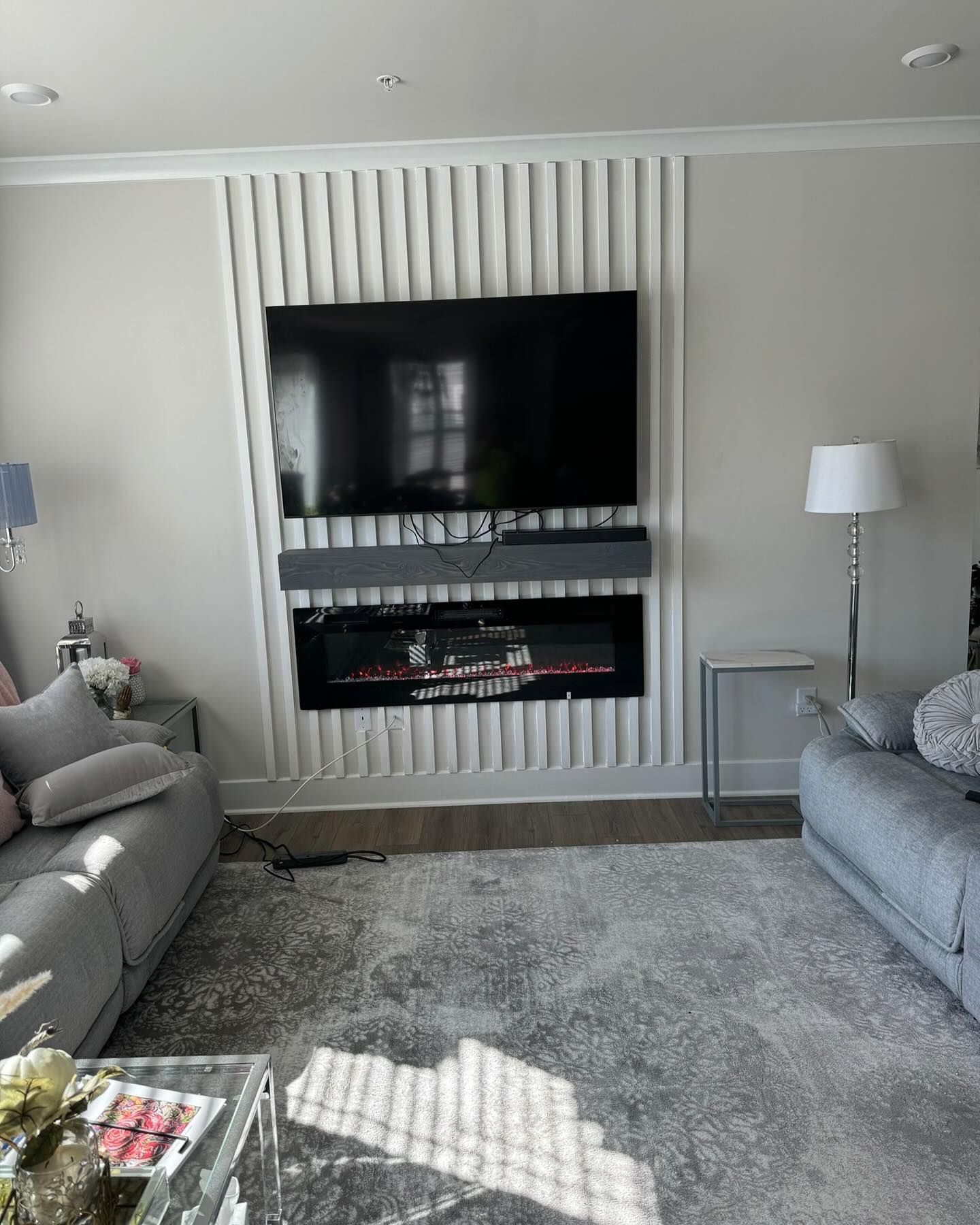 Living room with a modern fireplace, TV, soundbar, and gray sofas. Light gray walls, rug.