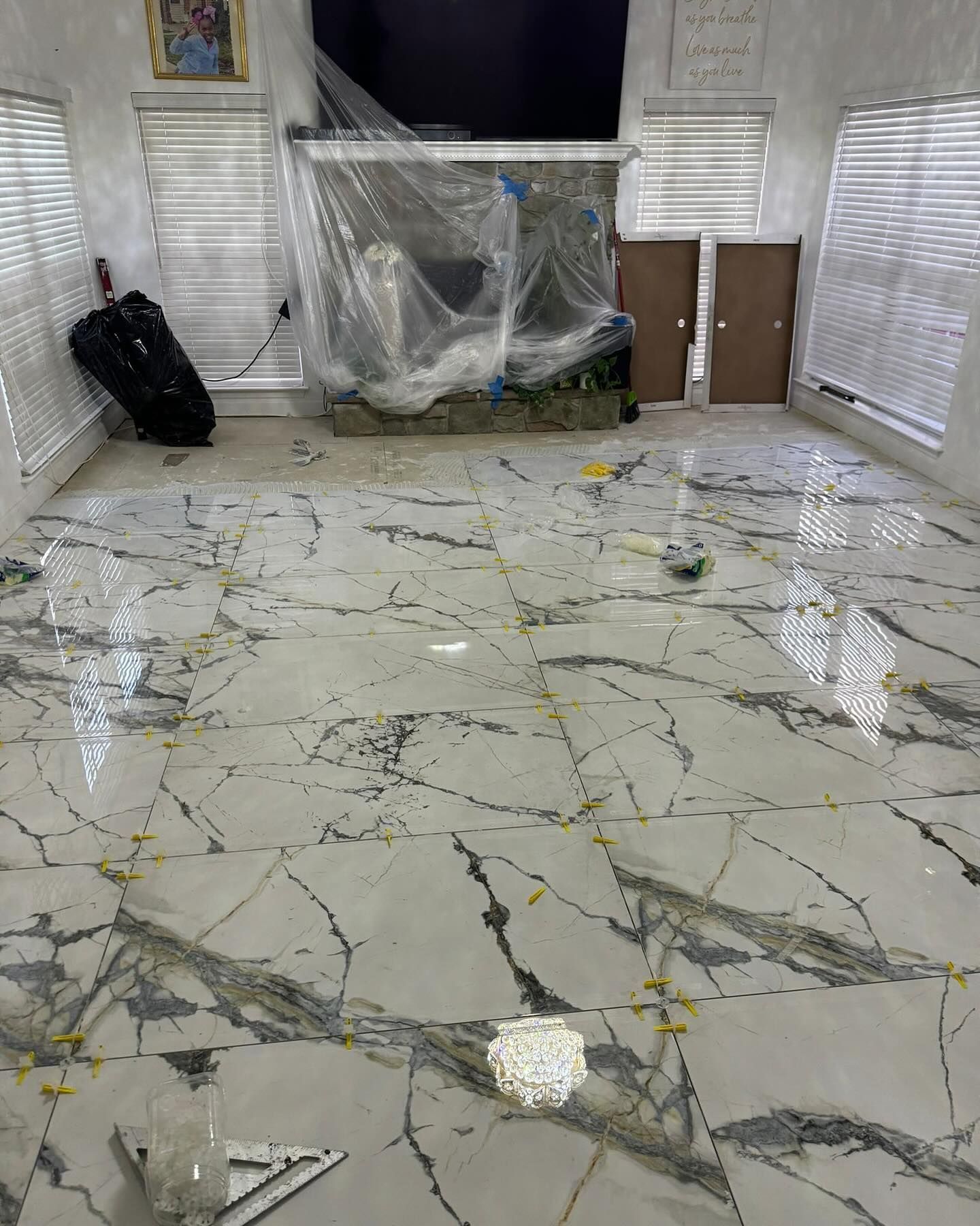 Tiled room with large white and gray patterned tiles, blinds on windows, furniture covered in plastic.