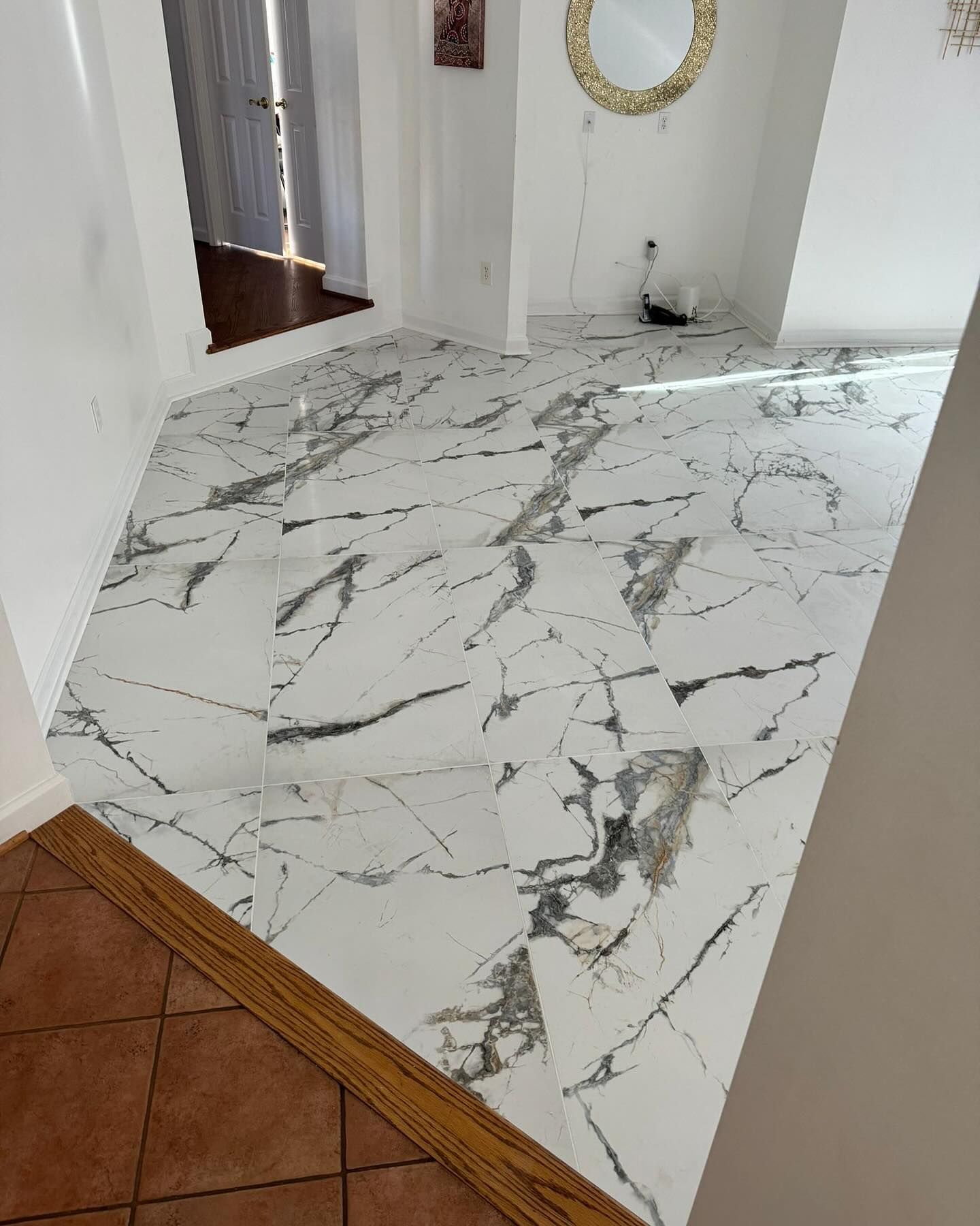 White marble-patterned tile floor in a hallway, leading to a door; brown wood trim, white walls.