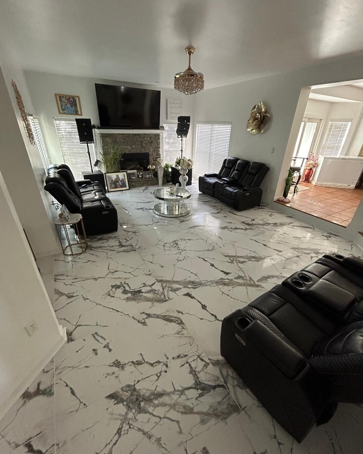 Spacious living room with marble floors, black leather recliners, fireplace, and large TV.