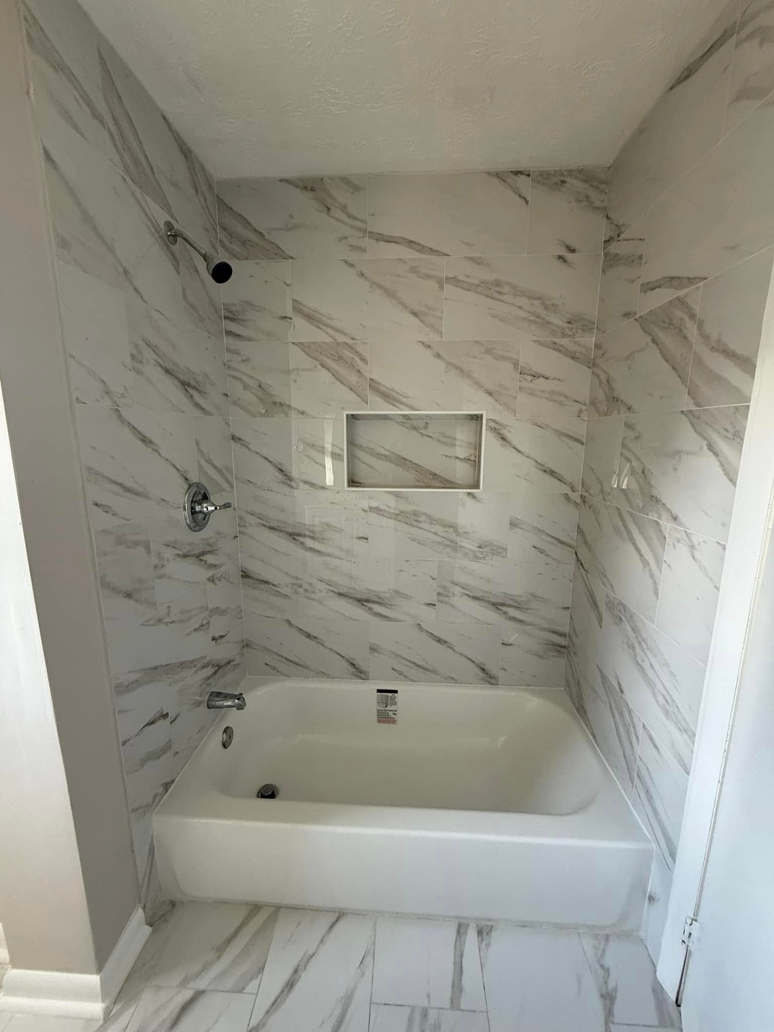 White bathroom with marble-look tile, bathtub, and recessed shelf.