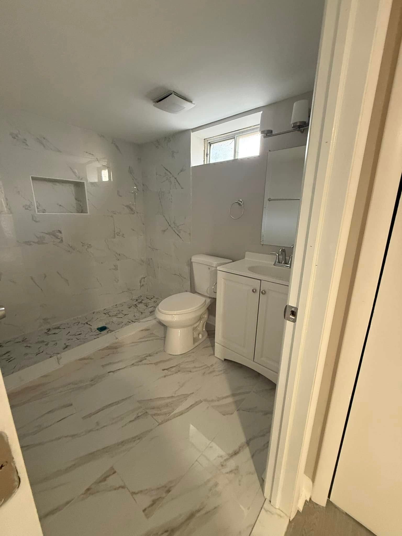 White bathroom with marble-look tile, a shower, toilet, and vanity.