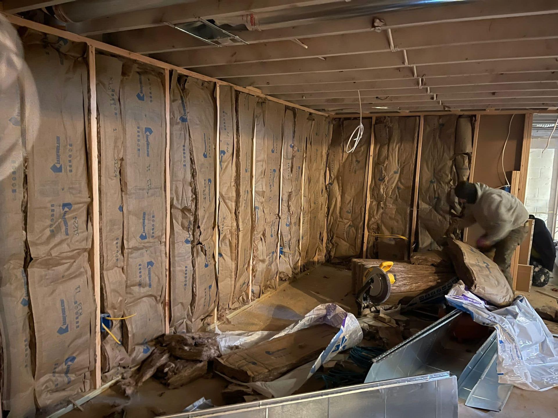 Interior view of a room under construction with exposed insulation in the walls. A person is working in the room.
