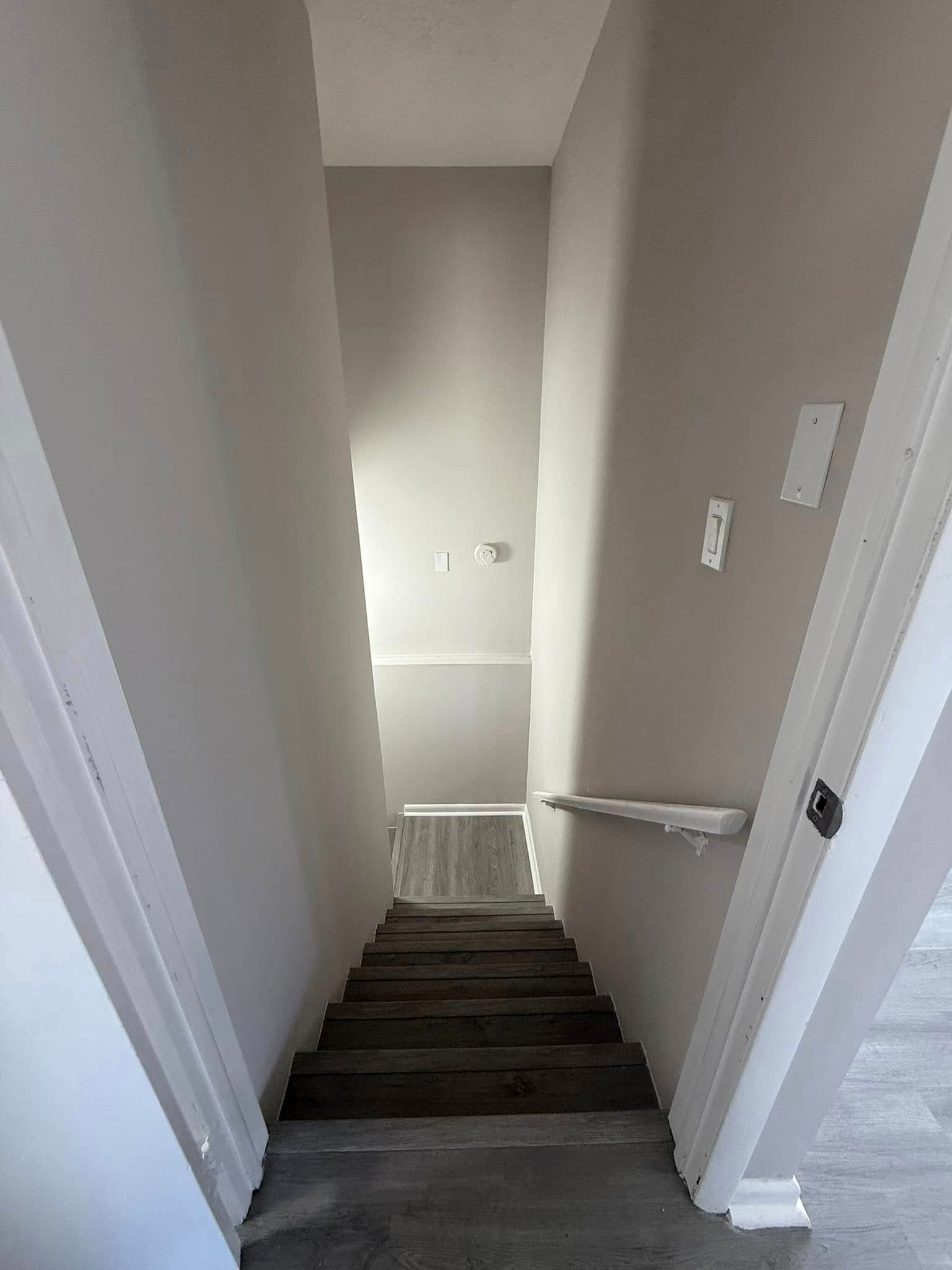 Staircase viewed from the top. Gray steps, white and gray walls. Doorways on either side of the top.